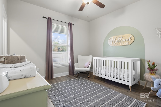 bedroom featuring dark hardwood / wood-style flooring, a crib, and ceiling fan