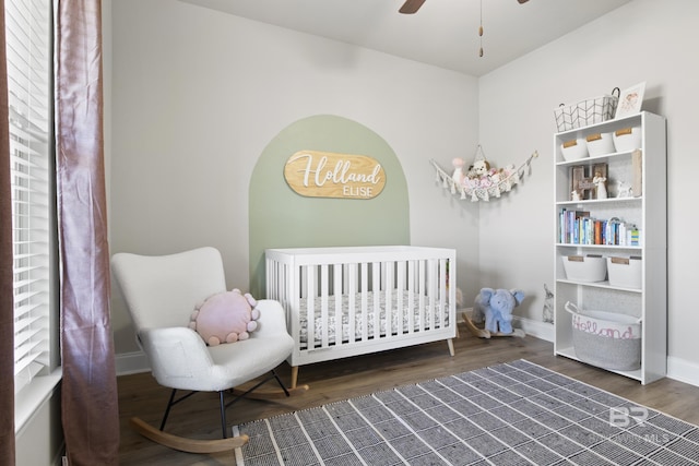 bedroom with a crib, dark hardwood / wood-style floors, and ceiling fan