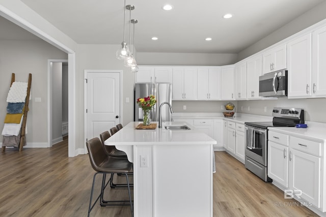 kitchen featuring sink, appliances with stainless steel finishes, white cabinets, a center island with sink, and decorative light fixtures