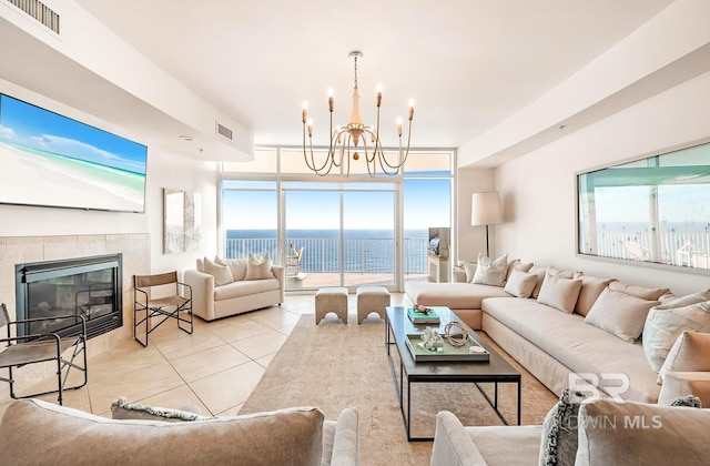 living room with light tile patterned flooring, a wall of windows, a notable chandelier, a water view, and a tiled fireplace