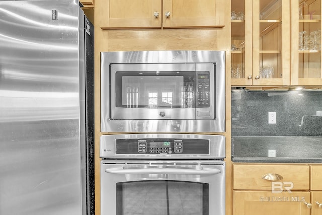 room details with stainless steel appliances, dark countertops, and glass insert cabinets