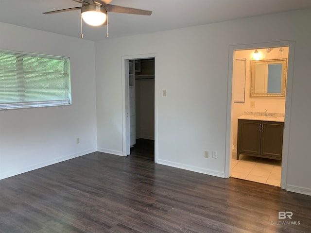 unfurnished bedroom with a closet, connected bathroom, a spacious closet, and dark hardwood / wood-style flooring