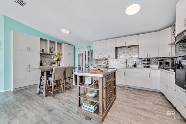 kitchen featuring a center island, open shelves, light countertops, decorative backsplash, and white cabinetry