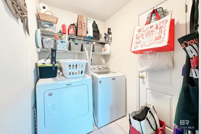 clothes washing area with laundry area, washing machine and dryer, light tile patterned floors, and a textured ceiling