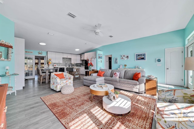 living room with lofted ceiling, light wood-type flooring, visible vents, and ceiling fan