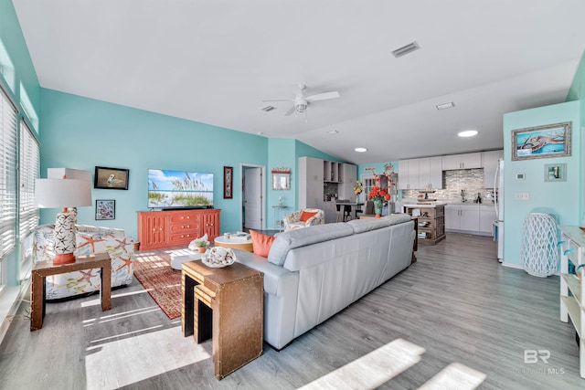 living room with vaulted ceiling, ceiling fan, light wood-style flooring, and visible vents