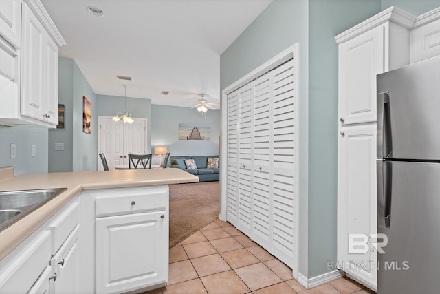 kitchen featuring stainless steel fridge, light tile patterned floors, white cabinets, and ceiling fan with notable chandelier