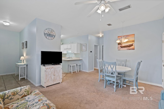 dining space featuring light carpet, ceiling fan with notable chandelier, and sink