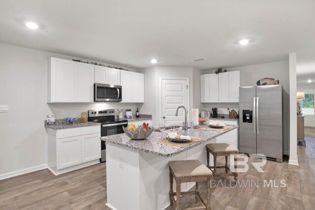 kitchen featuring white cabinetry, sink, an island with sink, appliances with stainless steel finishes, and light wood-type flooring