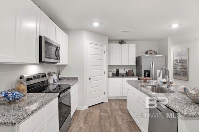 kitchen with sink, stainless steel appliances, an island with sink, light hardwood / wood-style floors, and white cabinets