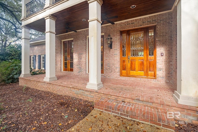 view of exterior entry featuring covered porch, ceiling fan, and a balcony