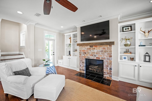 living area featuring dark wood-type flooring, visible vents, a ceiling fan, and a fireplace