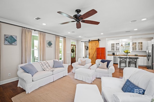 living area with ornamental molding, a barn door, visible vents, ceiling fan, and wood finished floors