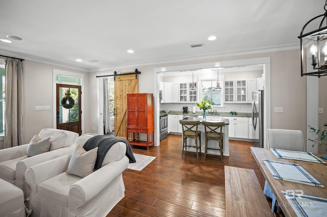 living area with dark wood-type flooring, recessed lighting, ornamental molding, and a barn door