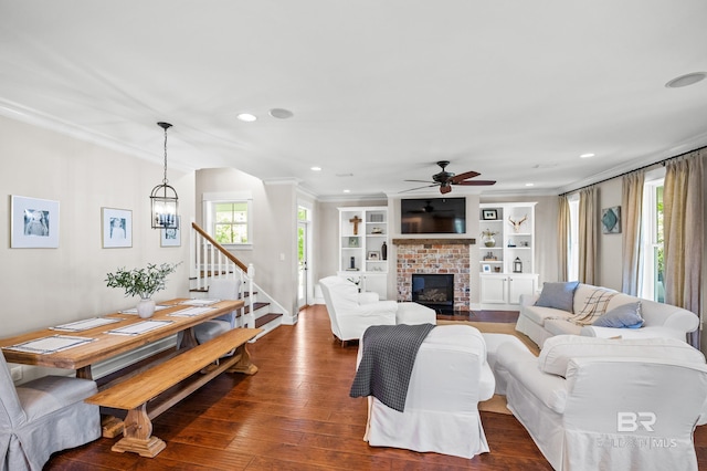 living room with crown molding, ceiling fan, a fireplace, dark wood-type flooring, and stairway