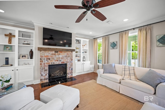 living room featuring crown molding, ceiling fan, a fireplace, visible vents, and wood finished floors