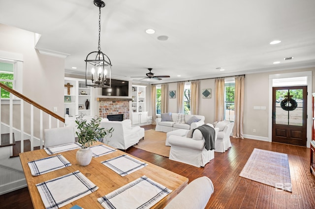living room featuring dark wood-style flooring, a healthy amount of sunlight, crown molding, and ceiling fan with notable chandelier