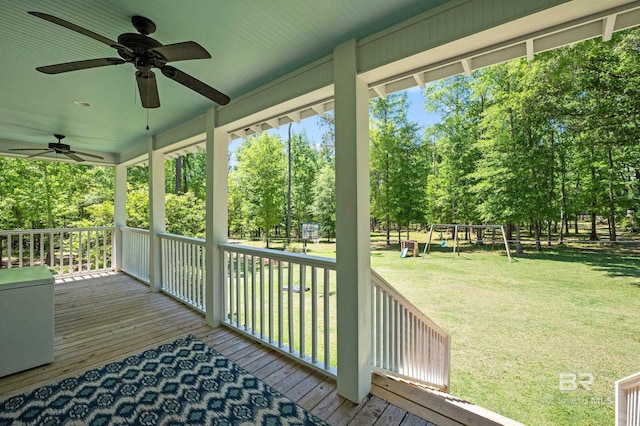 wooden terrace with a ceiling fan, a playground, and a lawn