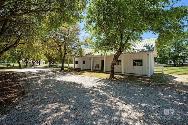view of front of house featuring board and batten siding, gravel driveway, a standing seam roof, metal roof, and fence