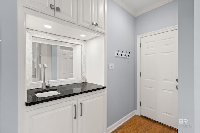 bar with crown molding, baseboards, a sink, and light wood-style flooring