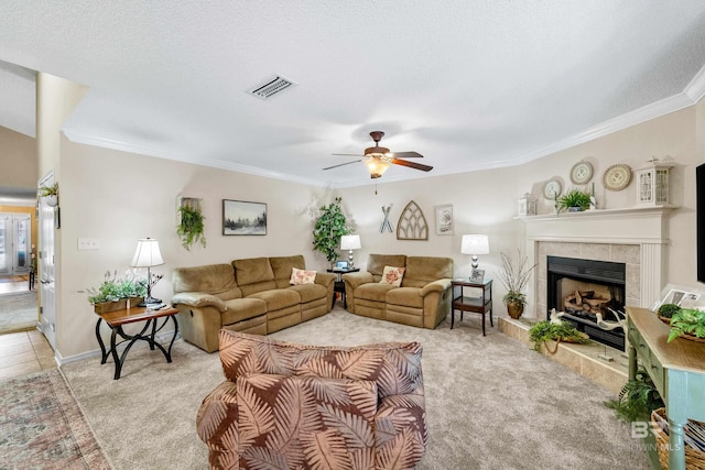 carpeted living room with ceiling fan, ornamental molding, a textured ceiling, and a tiled fireplace