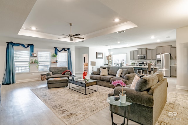living area with crown molding, plenty of natural light, a raised ceiling, and light wood finished floors