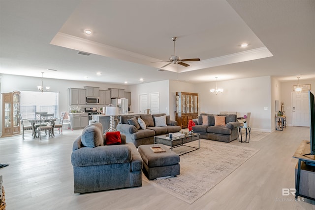 living area featuring crown molding, a raised ceiling, ceiling fan with notable chandelier, and light wood-style flooring