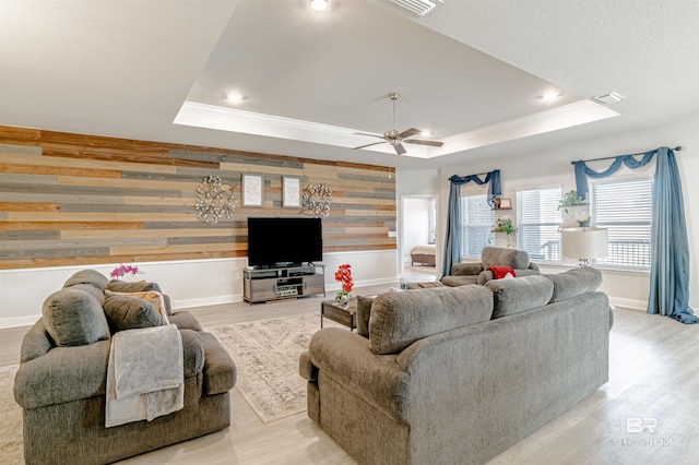 living area featuring wooden walls, crown molding, light wood finished floors, and a raised ceiling