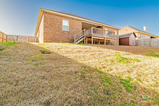 rear view of property featuring a wooden deck, a fenced backyard, a storage unit, brick siding, and stairway