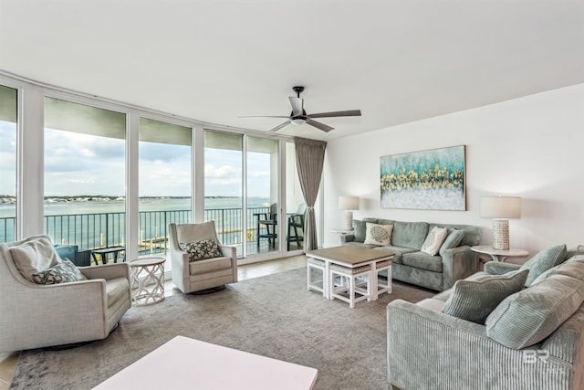 living area featuring ceiling fan, a wall of windows, and a water view