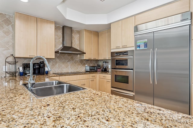 kitchen with a sink, stainless steel appliances, wall chimney range hood, and light brown cabinets