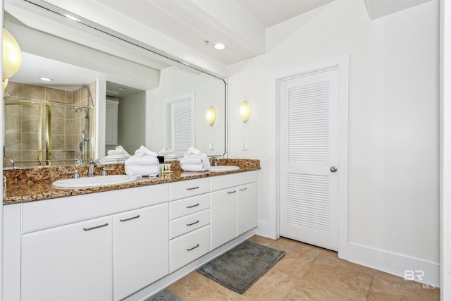 bathroom featuring double vanity, a stall shower, baseboards, and a sink