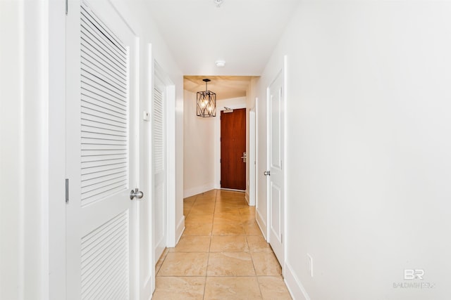 corridor featuring a chandelier, baseboards, and light tile patterned floors