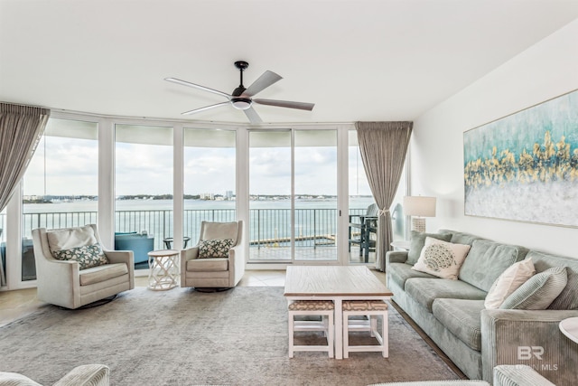 carpeted living room featuring a wall of windows, a water view, and a ceiling fan