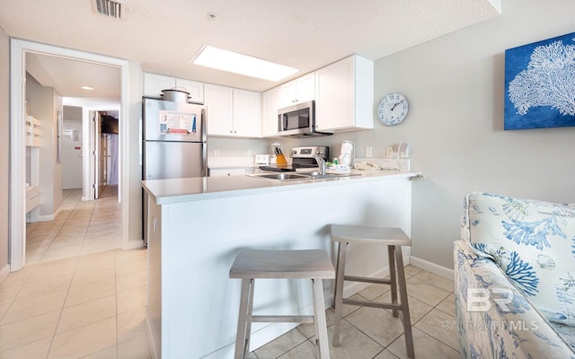 kitchen with white cabinets, appliances with stainless steel finishes, kitchen peninsula, and a kitchen breakfast bar