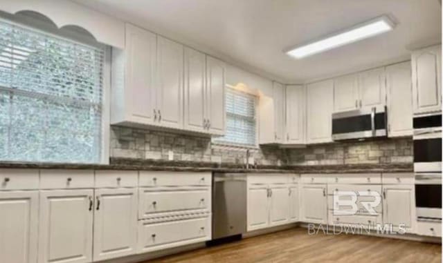 kitchen with stainless steel appliances, white cabinetry, light wood-type flooring, and decorative backsplash