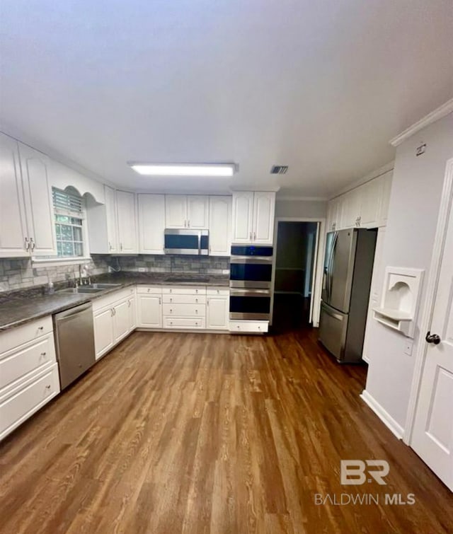 kitchen featuring appliances with stainless steel finishes, white cabinetry, sink, dark hardwood / wood-style flooring, and ornamental molding