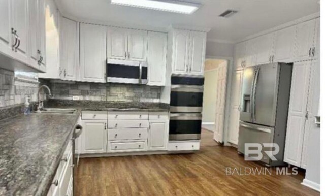 kitchen featuring sink, dark hardwood / wood-style flooring, stainless steel appliances, decorative backsplash, and white cabinets