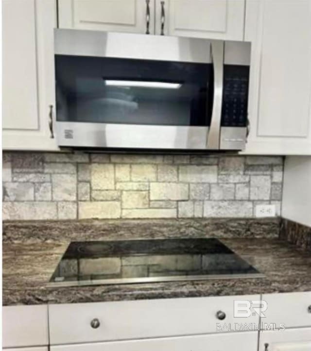 kitchen featuring black electric cooktop, backsplash, dark stone countertops, and white cabinets