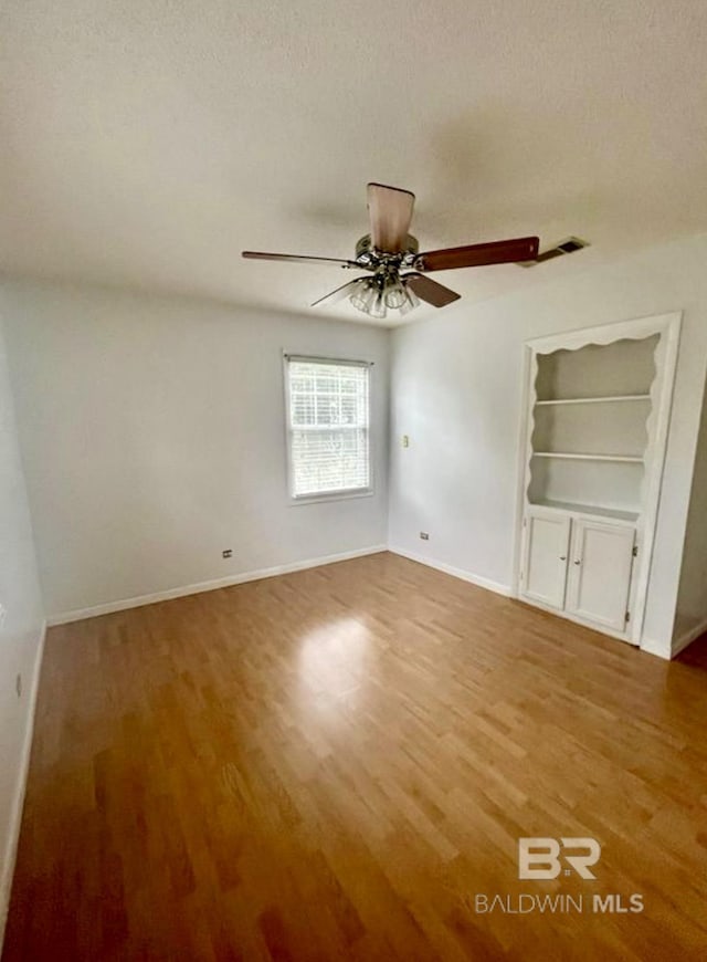 unfurnished room featuring hardwood / wood-style floors, built in shelves, a textured ceiling, and ceiling fan