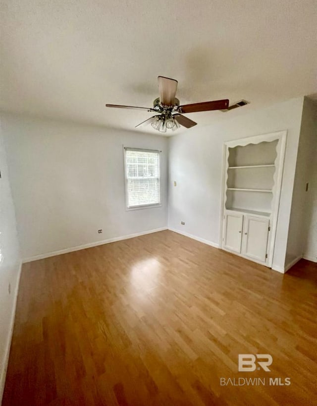 unfurnished room with hardwood / wood-style flooring, a textured ceiling, ceiling fan, and built in shelves