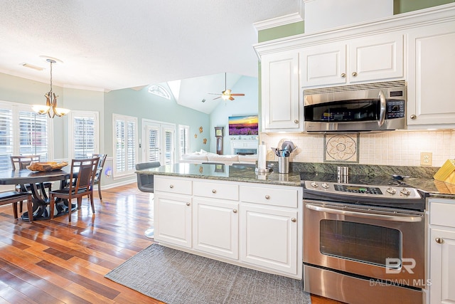 kitchen featuring hardwood / wood-style flooring, vaulted ceiling, white cabinetry, ceiling fan with notable chandelier, and appliances with stainless steel finishes