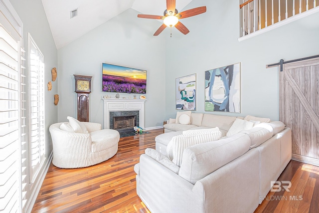 living room featuring high vaulted ceiling, ceiling fan, a barn door, and hardwood / wood-style floors