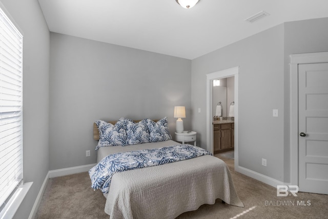 bedroom featuring connected bathroom and light colored carpet