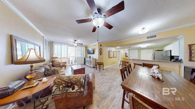 living room featuring crown molding, ceiling fan, light hardwood / wood-style floors, and a textured ceiling