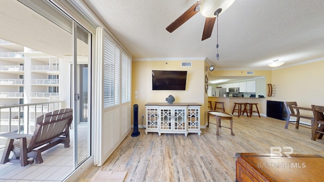 living room featuring ornamental molding, a textured ceiling, ceiling fan, and light hardwood / wood-style flooring