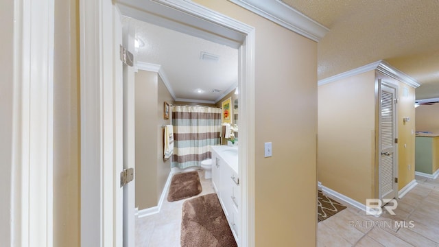 hall with light tile patterned floors, ornamental molding, and a textured ceiling