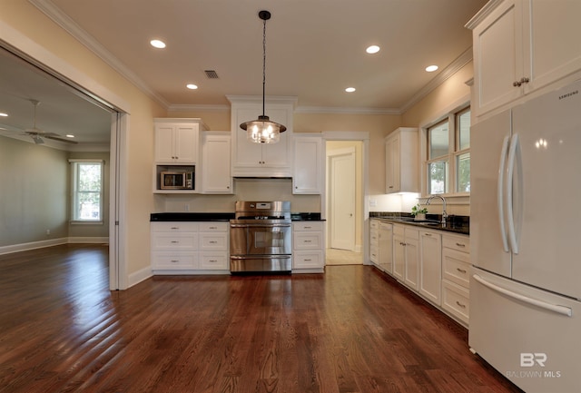 kitchen with white cabinets, appliances with stainless steel finishes, dark countertops, dark wood finished floors, and crown molding