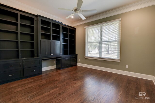 unfurnished office with ornamental molding, built in desk, dark wood-style flooring, and baseboards