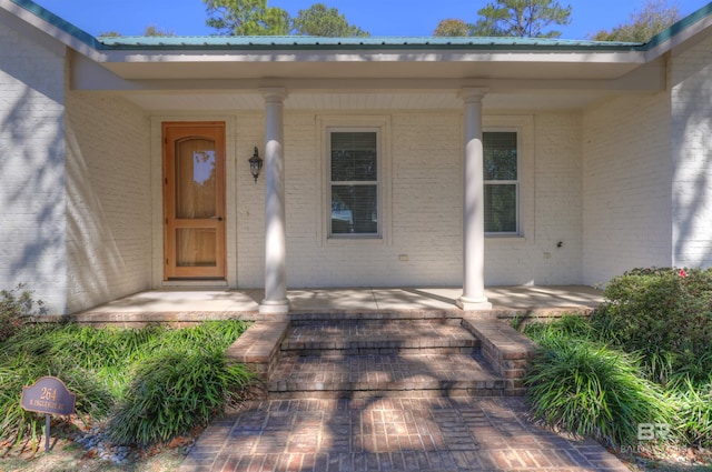 doorway to property featuring metal roof, a porch, and brick siding